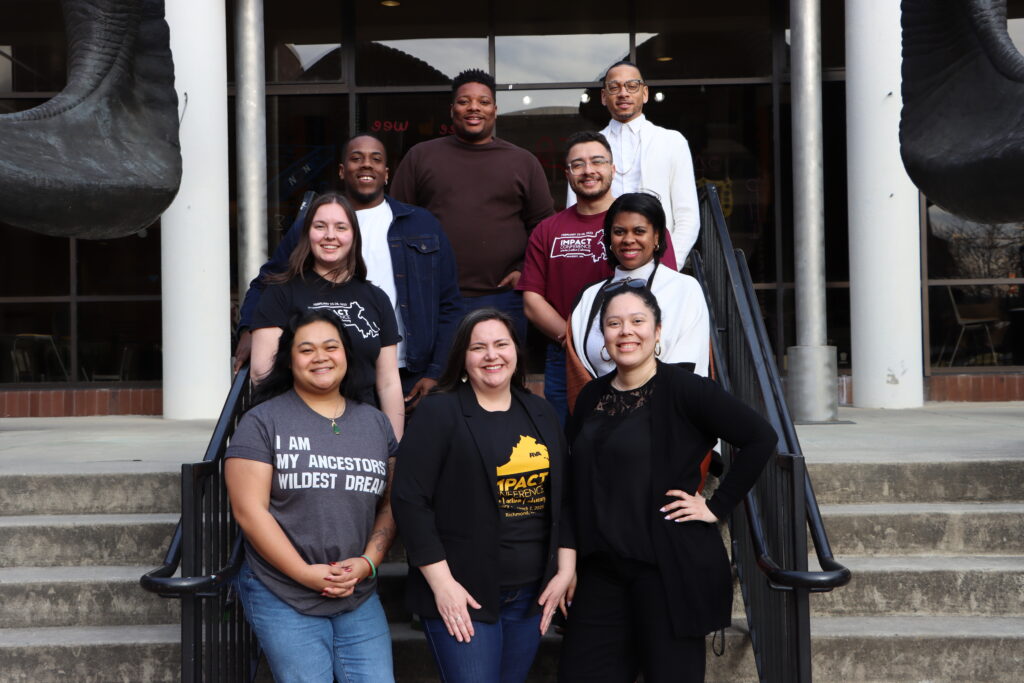 9 IMPACT Board members smiling, standing on stairs.